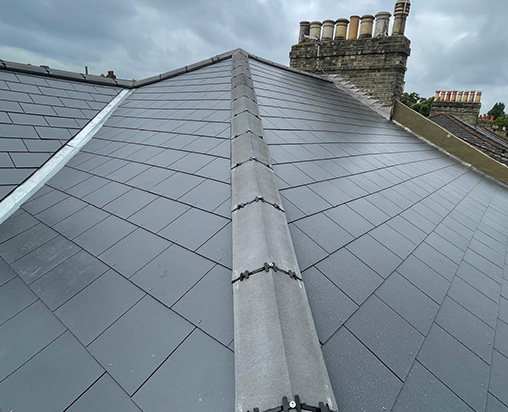 Slate roof installation with chimney and cloudy sky in the background.