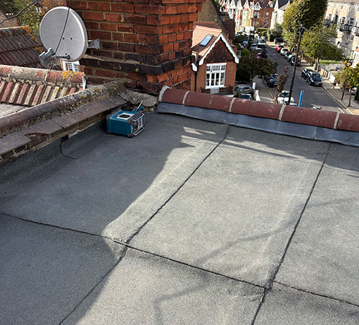 Flat roofing surface with a chimney and satellite dish in a residential area.