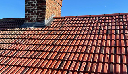 Tiled roof with chimney against a clear blue sky, showcasing quality roofing work.