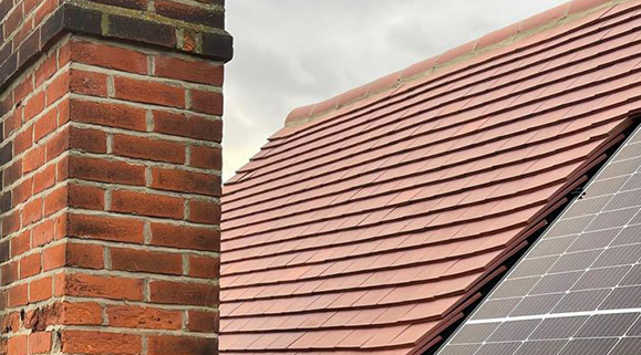 Tiled roof section with a brick chimney and solar panels under cloudy sky