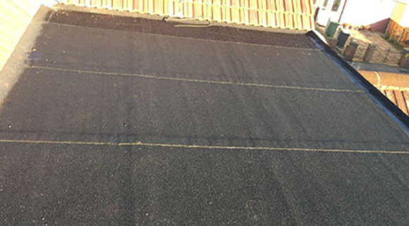 Flat roofing installation showing dark roofing material across a residential building.