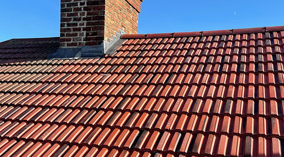 Tiled roof installation with chimney under clear blue sky