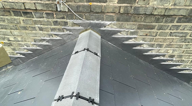 Close-up view of a slate roof with ridge tiles and brick wall background.