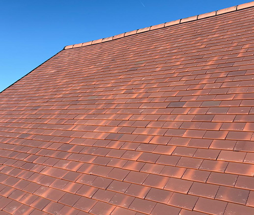 Red roof tiles on a sloped roof against a blue sky.
